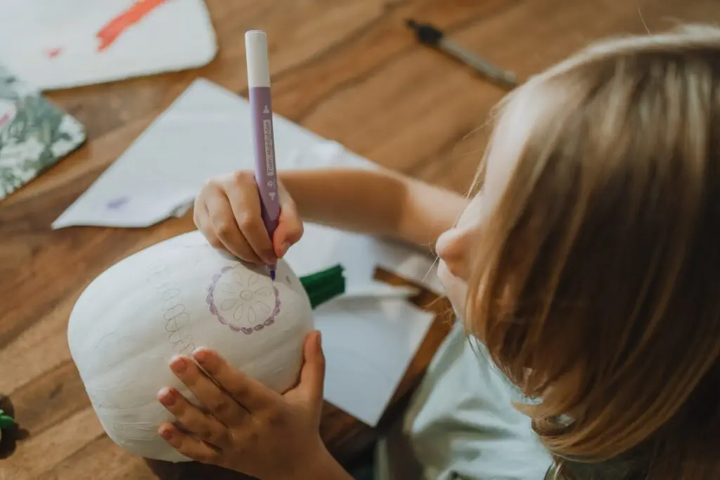 Une petite fille dessine un masque Mexicain sur une citrouille blanche.